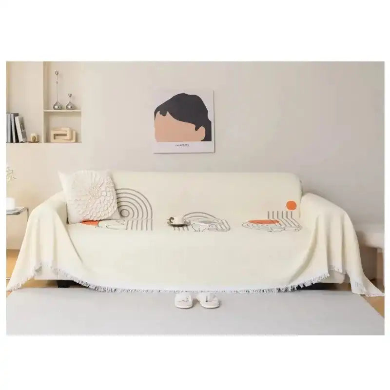 Cream sofa towel cover with abstract patterns and tassel edge, non-slip and breathable, enhancing a minimalist living room setup.