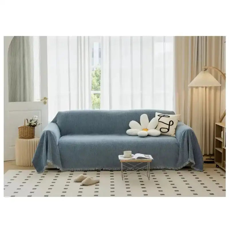 Blue solid non-slip sofa towel cover with tassel edge on a modern couch in a bright living room. Washable and breathable home decor cushion cover.