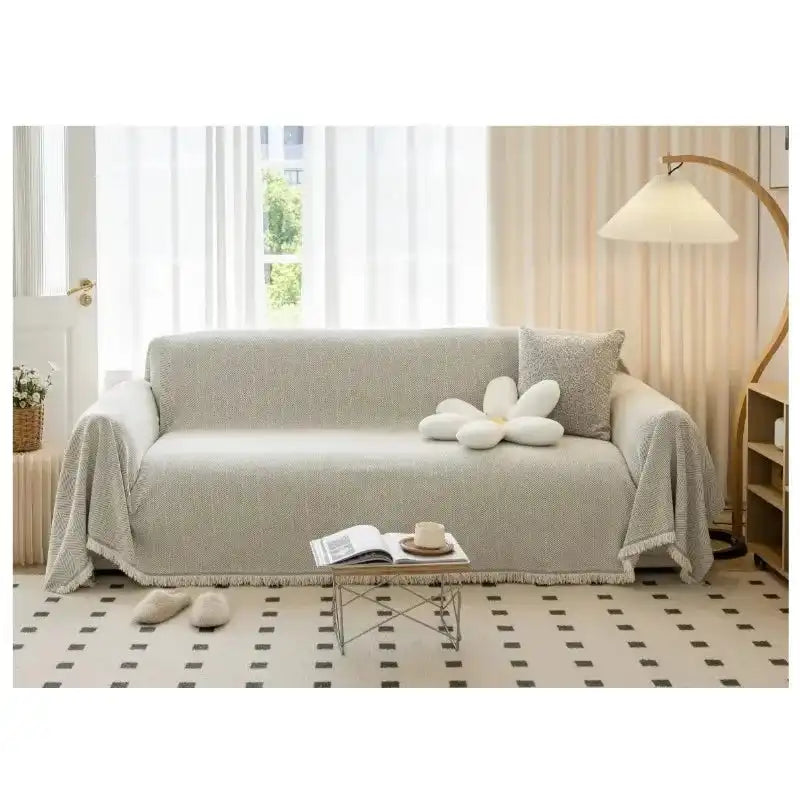 Beige sofa towel cover with tassel trim on a modern couch, offering a solid, breathable, and washable solution for home sofa protection.