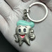 Gloved hand holding a smiling cartoon tooth keychain with teal hair, ideal as a dental hygiene or graduation gift for kids or moms.