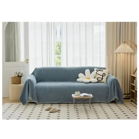Blue solid non-slip sofa towel cover with tassel edge on a modern couch in a bright living room. Washable and breathable home decor cushion cover.